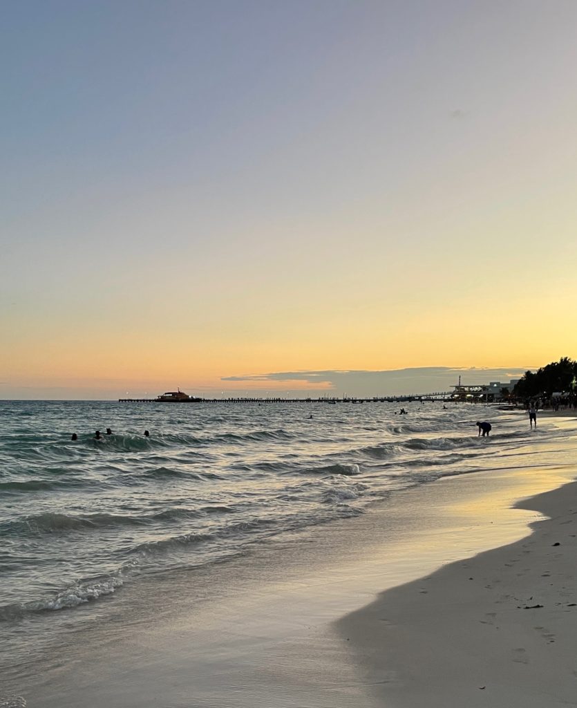 sunset on the main beach shore in Playa del carmen with a ferry parked in the distance