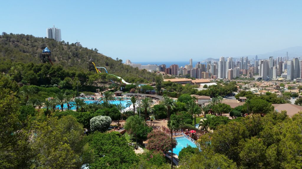 landscape photo of a water park many trees and several tall skyscrapers in the background  