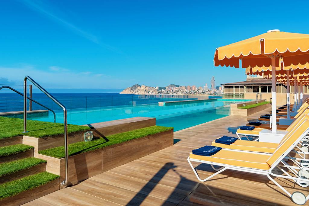 several beach lounge chairs and umbrellas on the terrace of h10 Porto Poniente hotel in Benidorm 