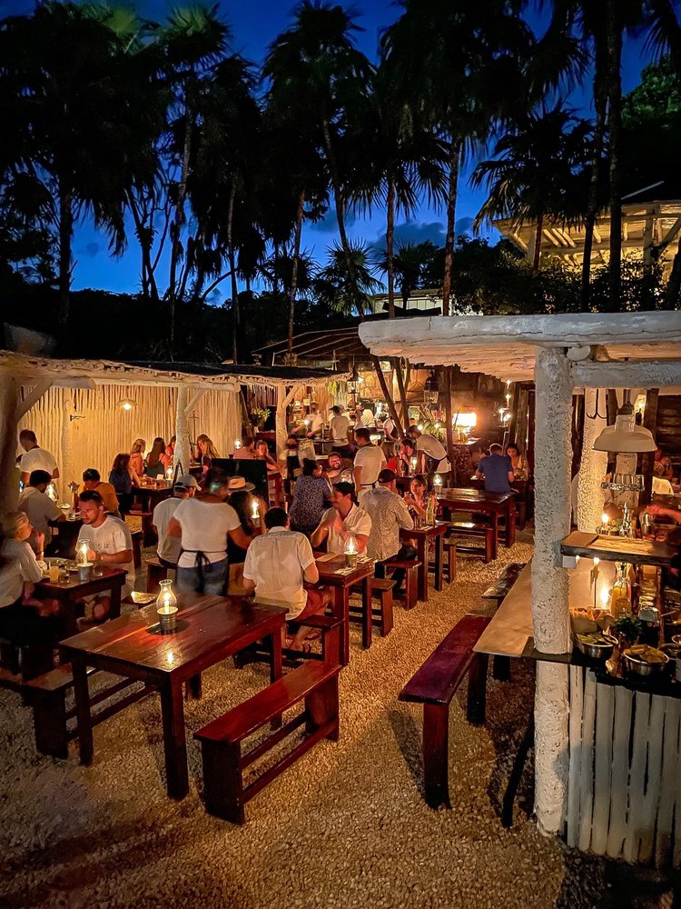 several wooden dining chairs in a open concept Hartwood restaurant surrounded by palm trees in Tulum, Mexico 