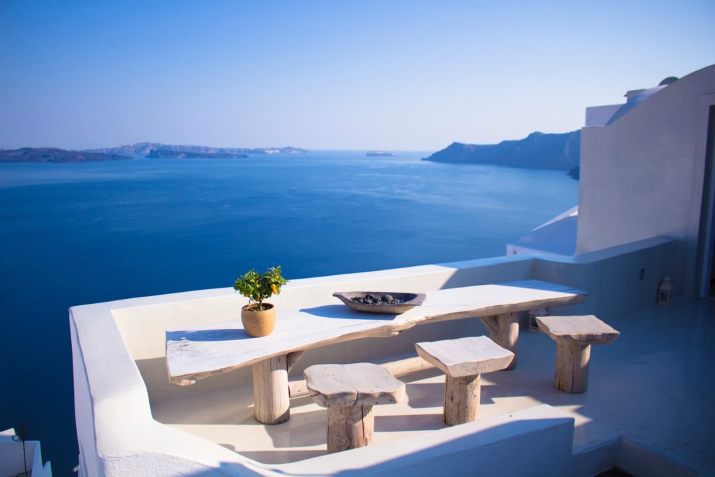 Ocean views from a classic white villa with three small tables on the balcony in Oia Greece