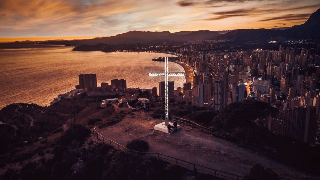 famous landmark named the cross sitting on a high mountain overlooking the city of Benidorm at sunset