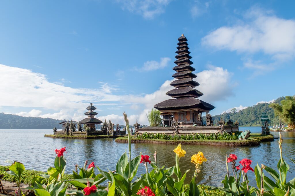 temple in the middle of the water located on a small island with flowers surrounding it in Bali Indonesia 
