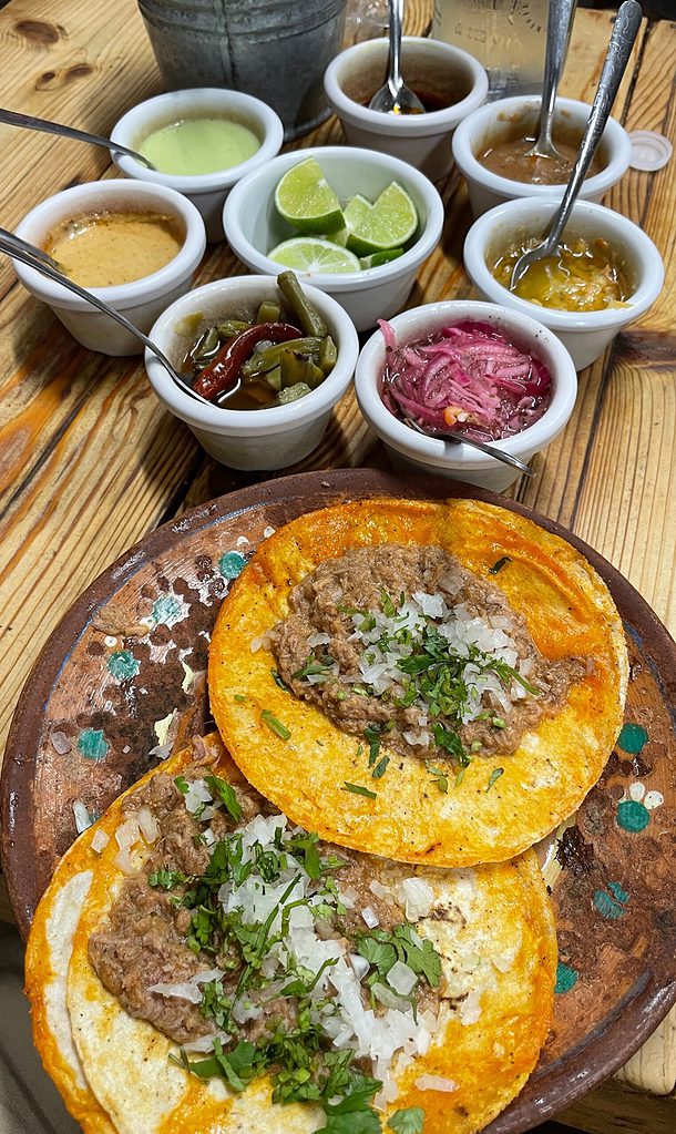 table full of birria style tacos with various small sides complimenting the birria tacos