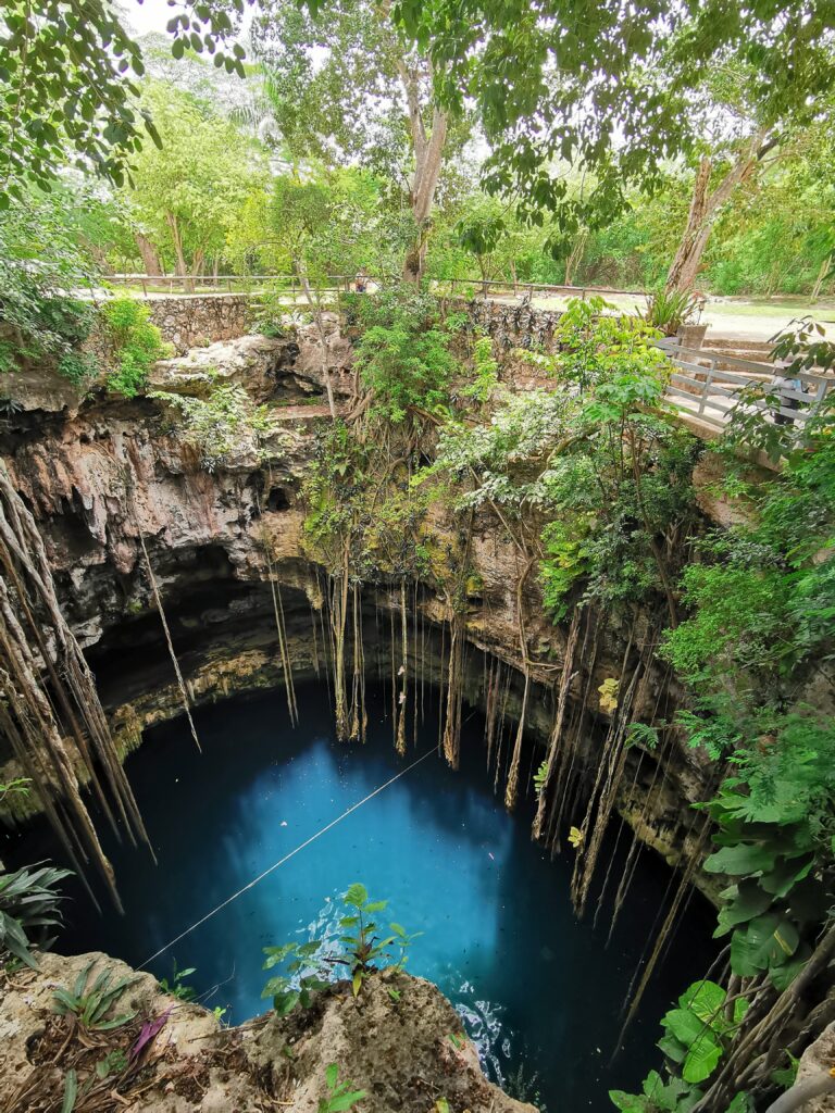 a deep blue crystal water sinkhole with bright green branches surrounding it, known as cenote lk kil in mexico