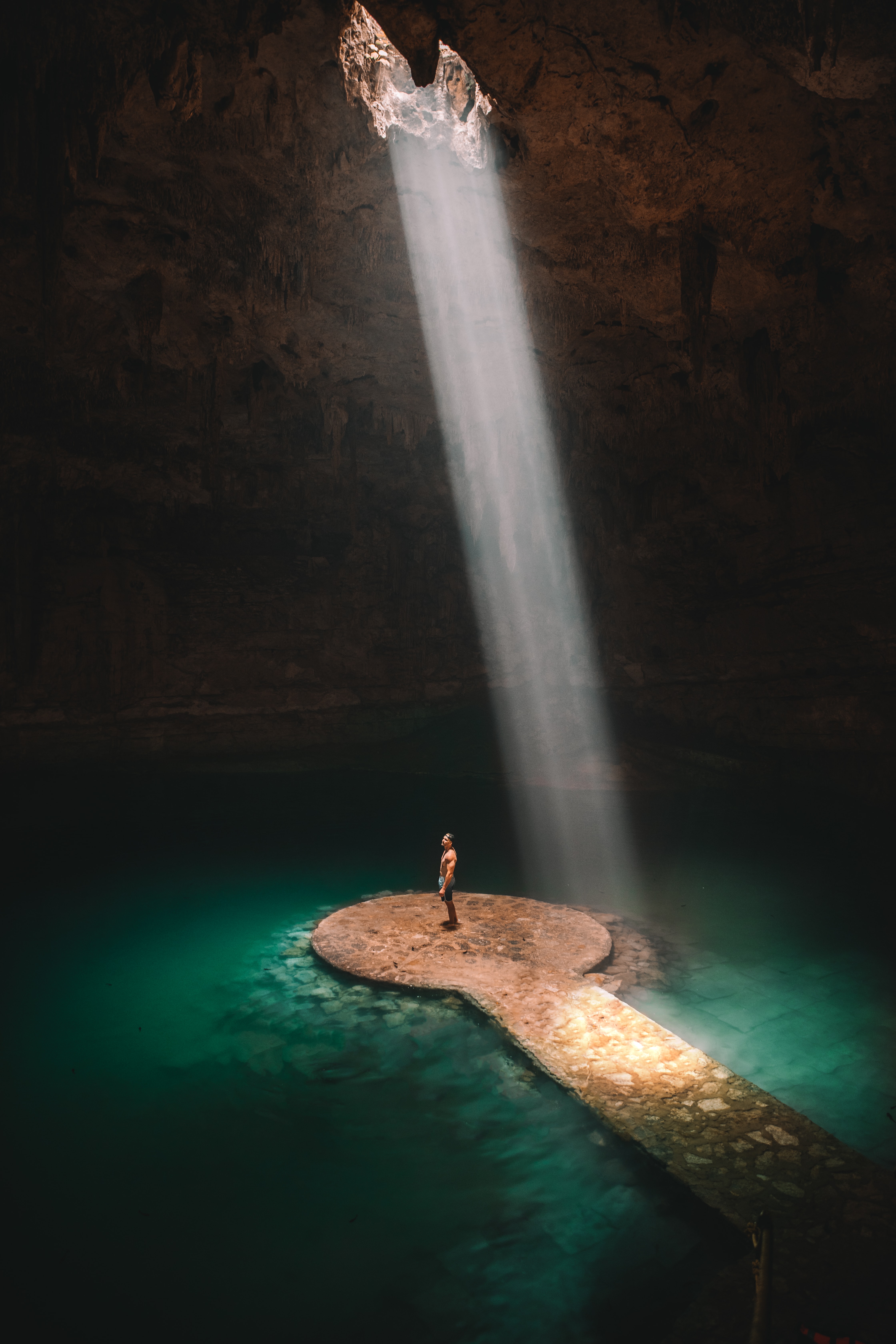 bright light beaming down straight in a underground dark cenote with clear walkway into the middle of the water