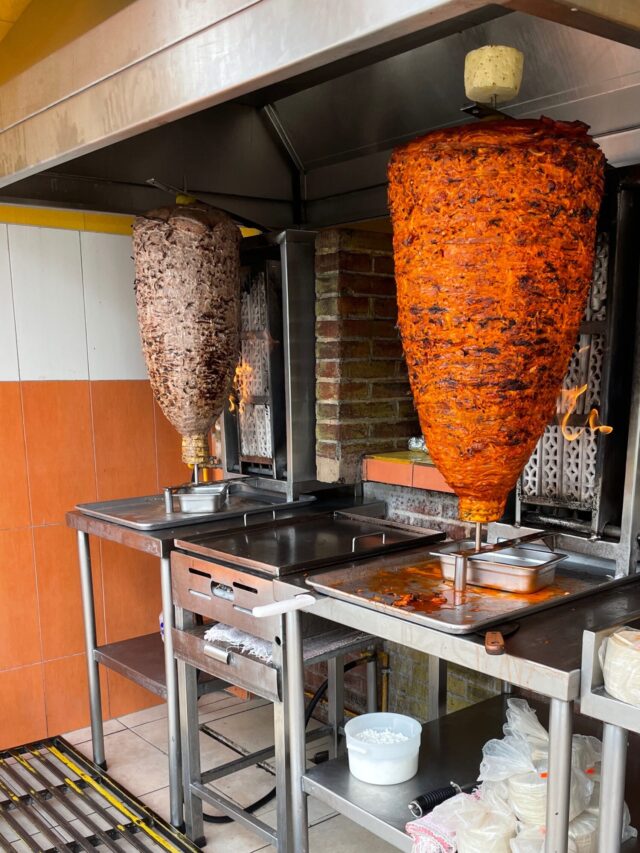 two very large spits of meat rotating making al pastor style meat for al pastor tacos