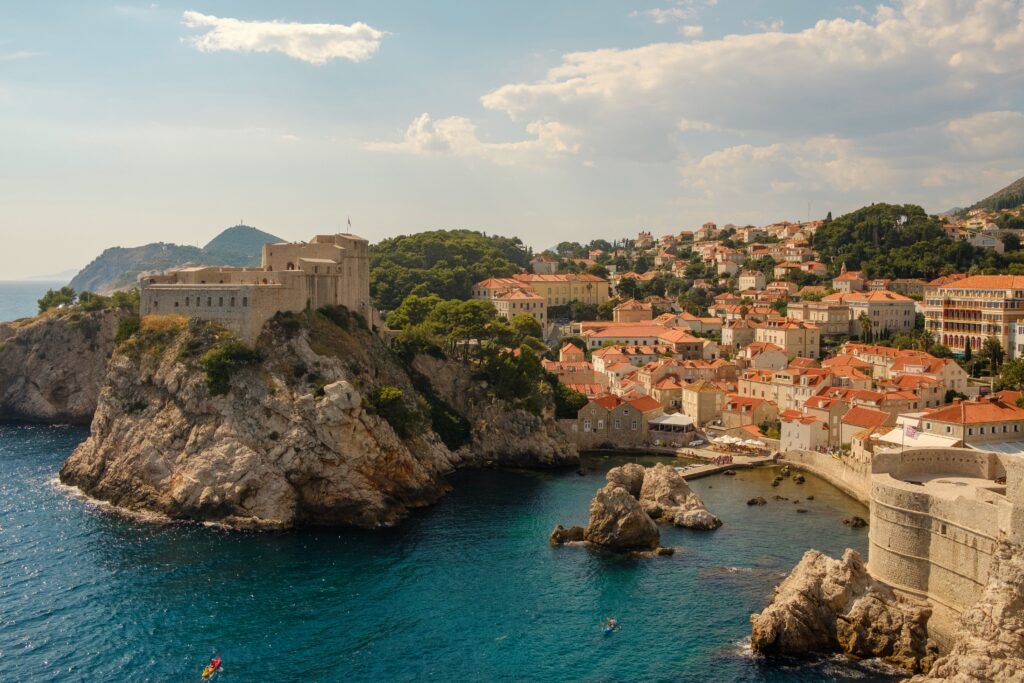 coastline of old traditional croatian homes alongside a coastline with a castle at the top of a hill above the water