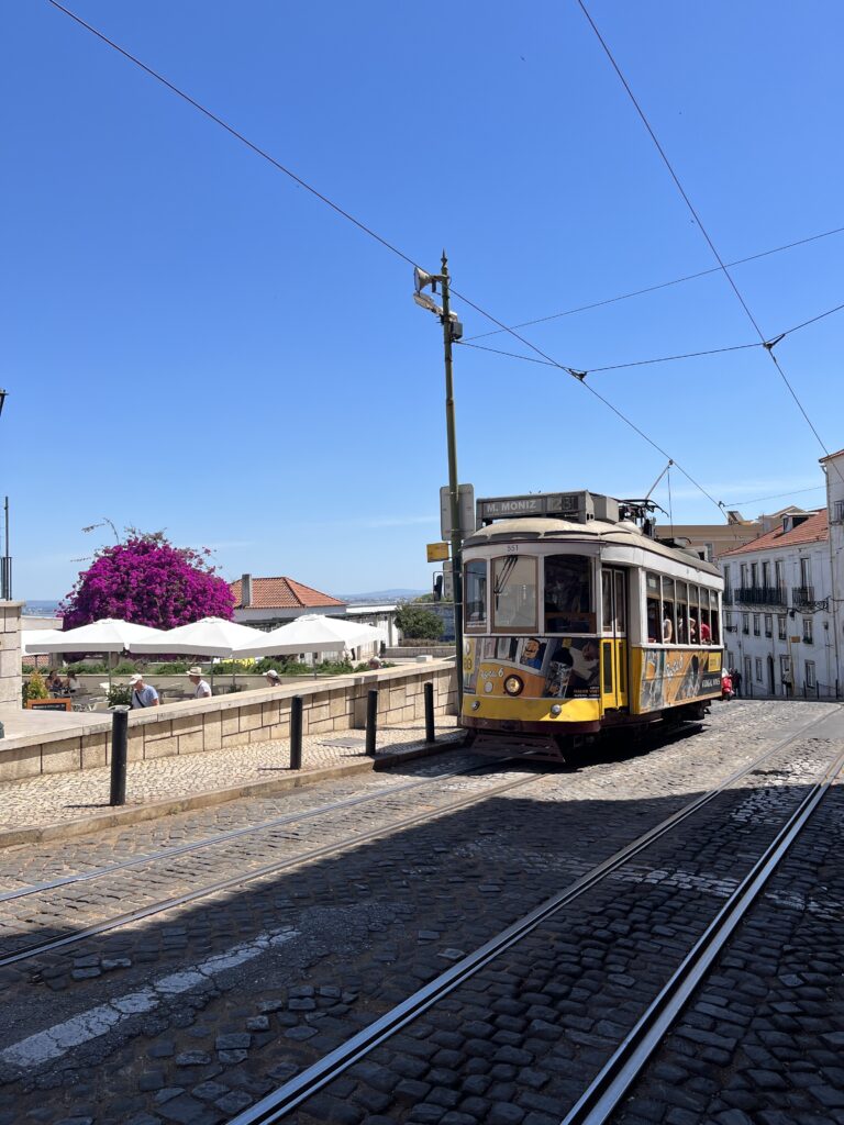 a yellow street car passing through the cobblestone streets in Lisbon, Portuagl