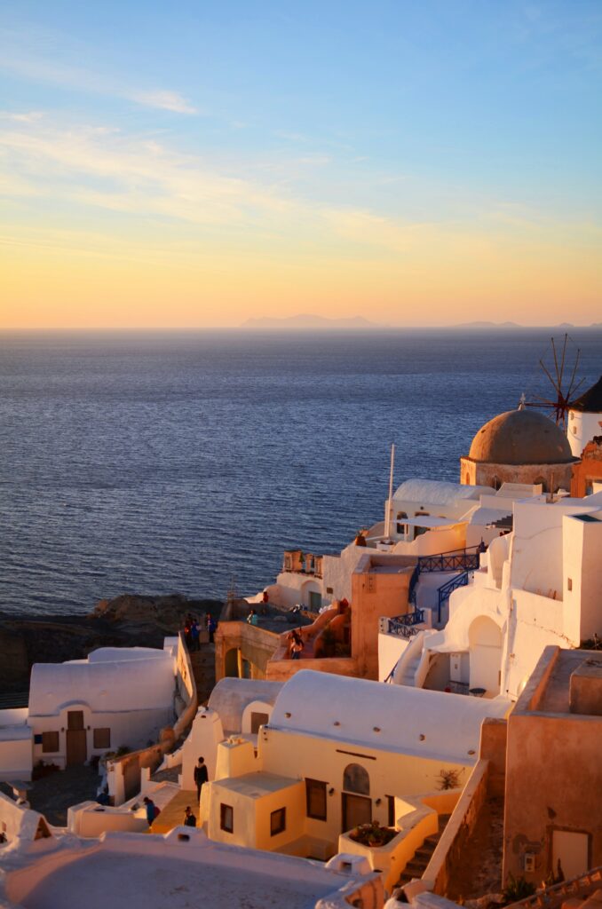 several classic white homes sitting on a hill above the ocean with a sunset in the background in oia greece