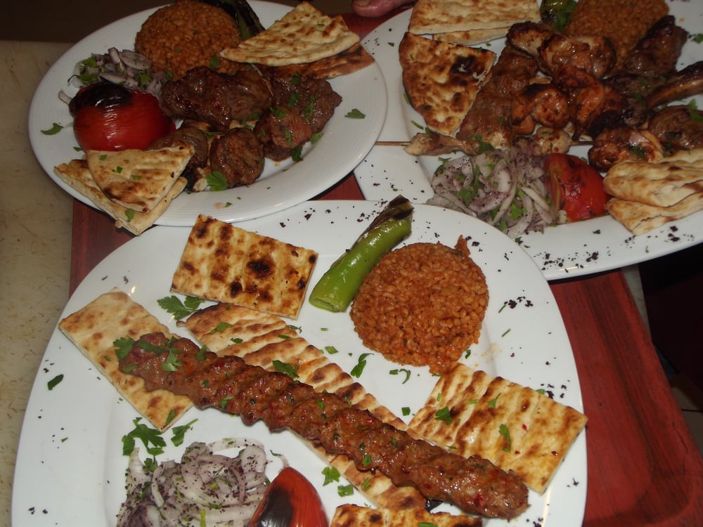 table of three plates full of various grilled meats, vegetables and turkish bread at otanik ocakbasi restaurant 
