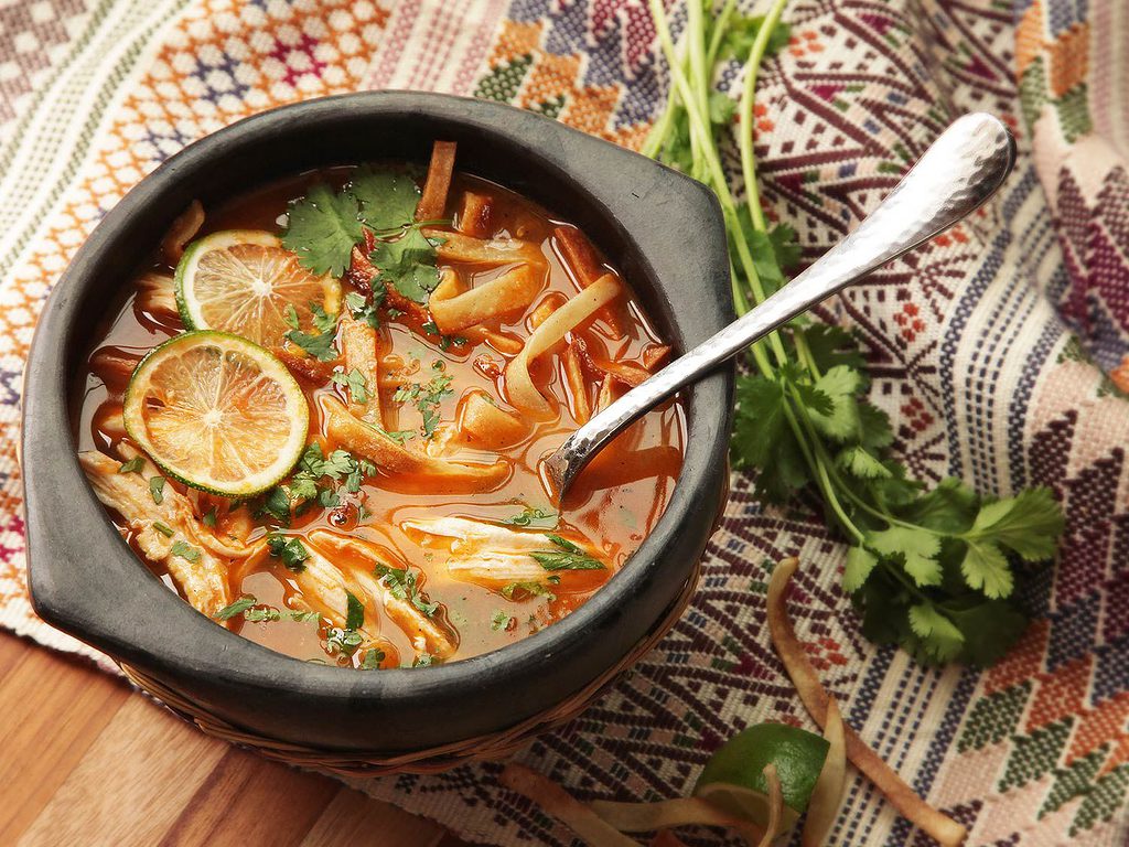 authentic mexican sopa de lima with sides of garnish beside of it