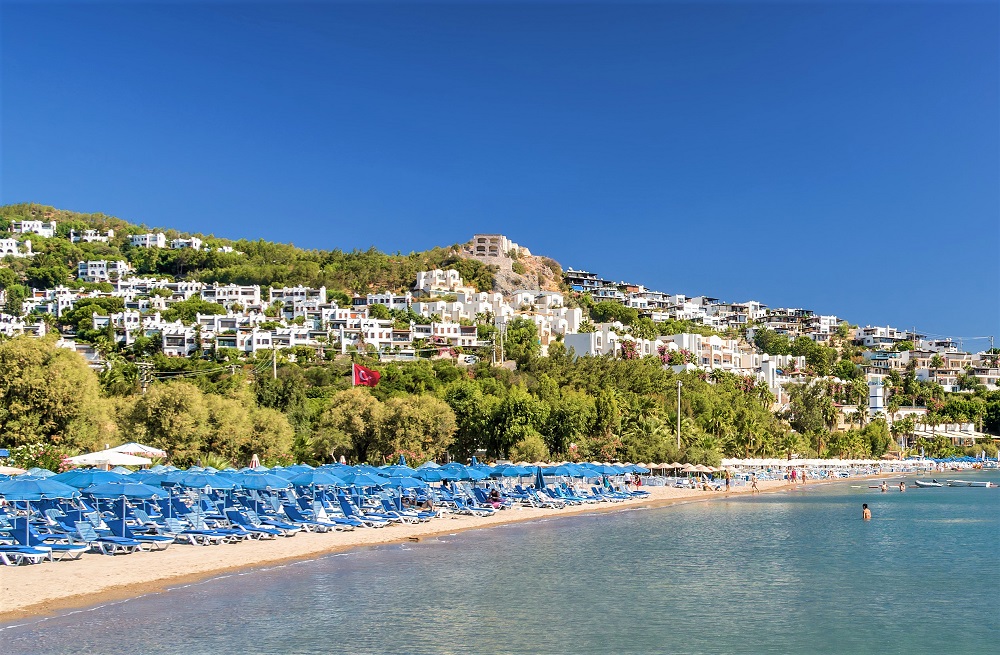 several blue umbrellas sitting along the shoreline of a beach in Bodrum Turkey 