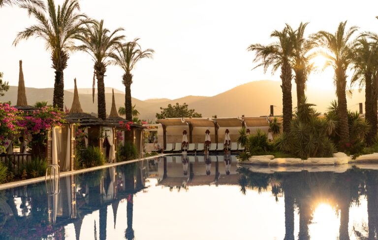 sunset at a hotel pool with palm trees and mountains in the background of bodrum turkey