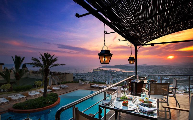 terrace with restaurant seating overlooking the hotel pool and city of bodrum with colourful sunset