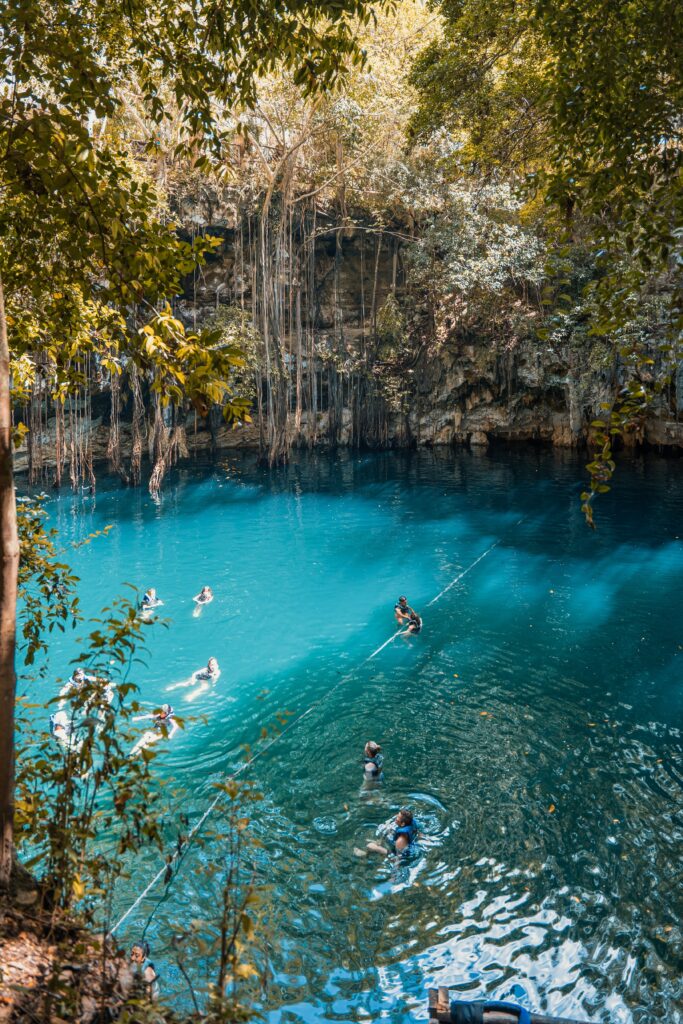 huge sinkhole cenote with crystal clear waters showing many swimming in the cool waters of cenote yokdzonot