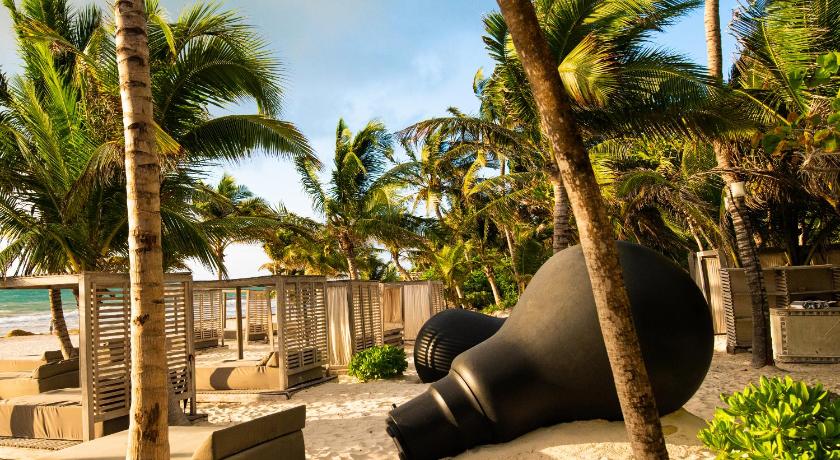 private beach area at casa malca beach club featuring lounge chairs with cabanas with massive lightbulbs as contemporary art