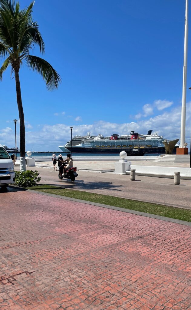 tourist walking on cobblestone streets on the island of cozumel in mexico with two large ferry ships docked at the island in the distance