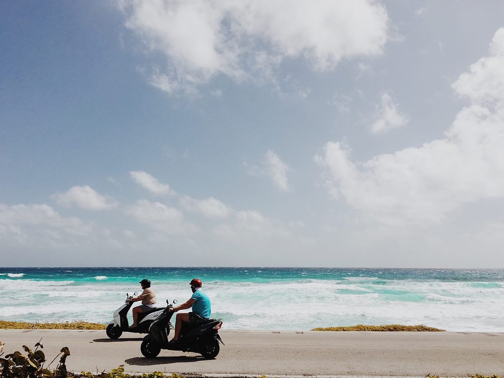 two individuals riding scooters on along the coastline of cozumel island in mexico
