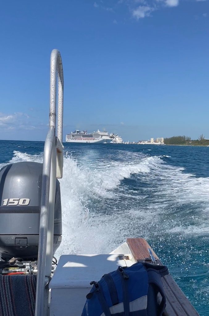 views of the back part of a boat making big wakes in the waters of Cozumel with a large cruise ship in the background docked