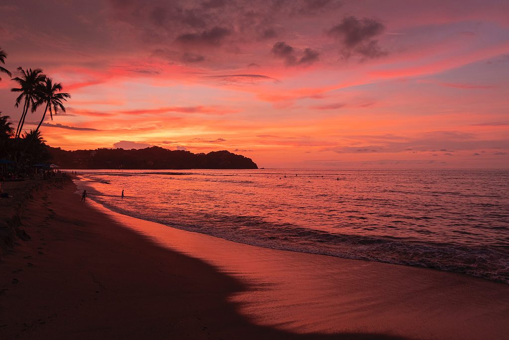a colourful sunset with various shades of pink setting in on a empty shoreline in Sayulita Mexico