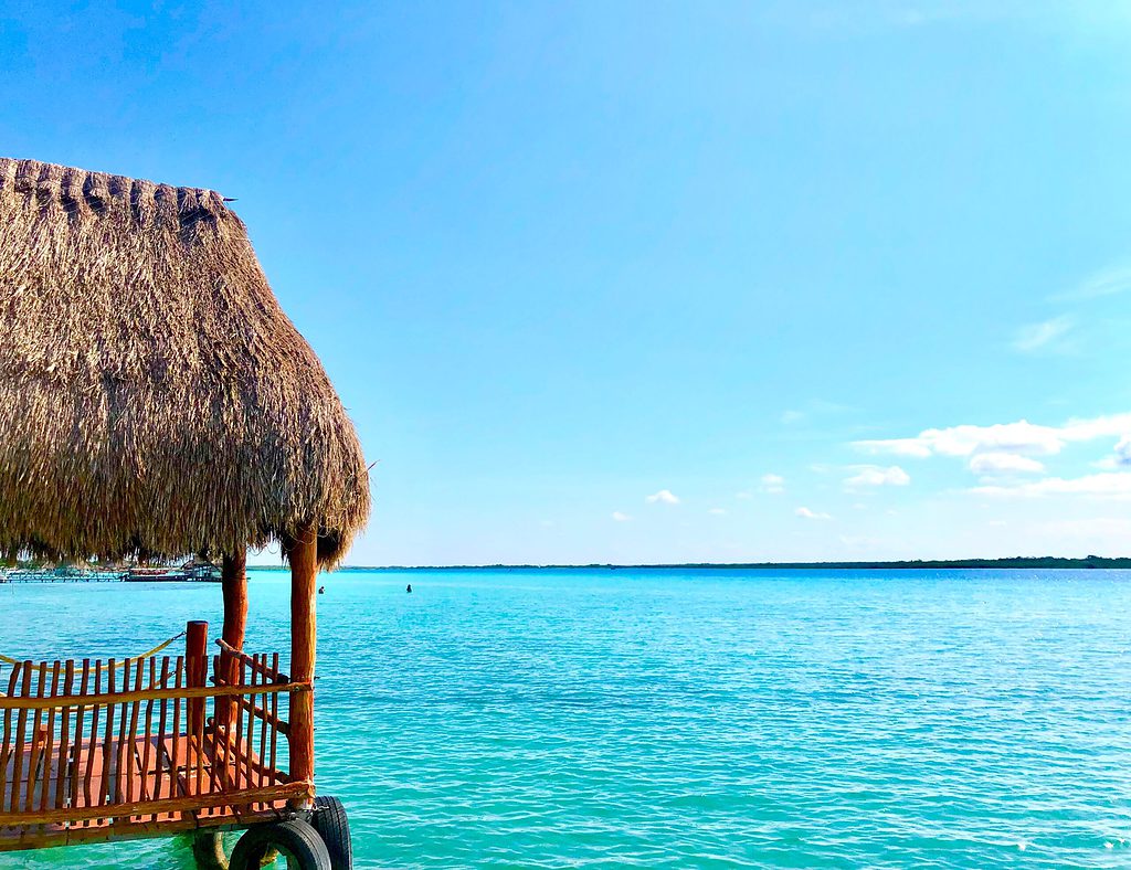 observation deck with a palapa roof with views o the Bacalar Lagoon featuring several shades of bright blue waters