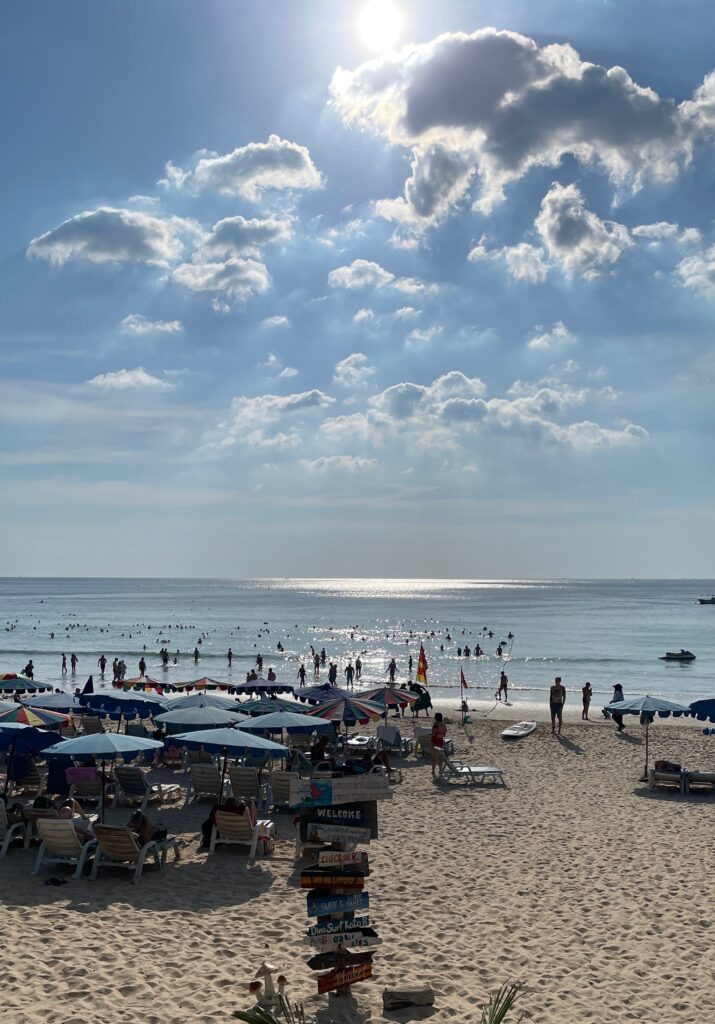 sun pealing through the clouds at a crowded Kata Beach in Phuket, Thailand