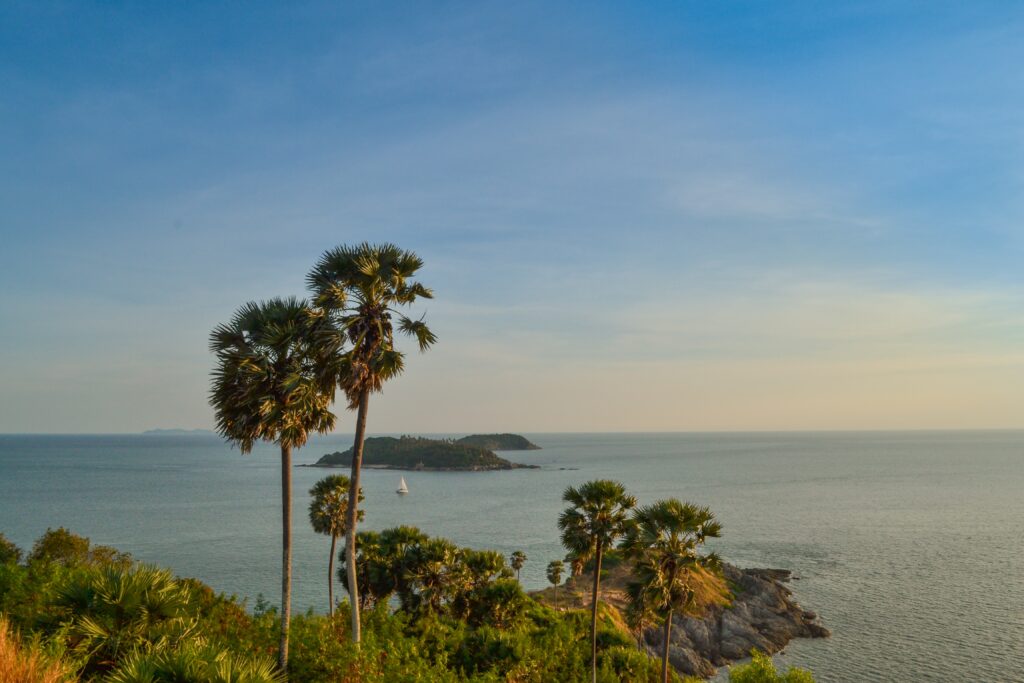 a sunset setting in amongst palm trees and islands at Cape Phrom Thep, a popular sunset spot in Phuket, Thailand 