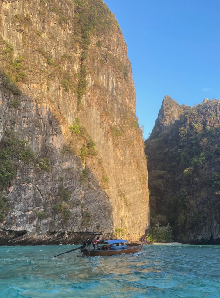 large limestone in the middle of the Andaman Sea with long tail boat going by at the Phi Phi islands in Thailand