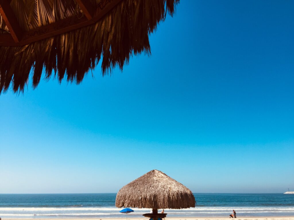 a quiet empty beach with several palapas on the beach shoreline in Ensenada, Mexico