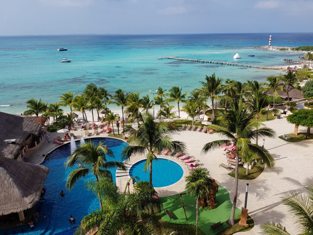 several palm trees around a pool and stunning turquoise waters at a resort in the Hotel Zone of Cancun, Mexico