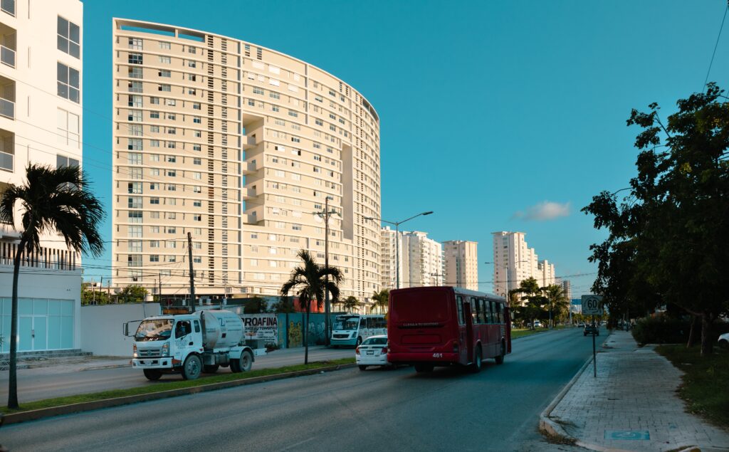 a street in Centro Cancun with a bus driving by and a few condos standing high as the sun beams on them 