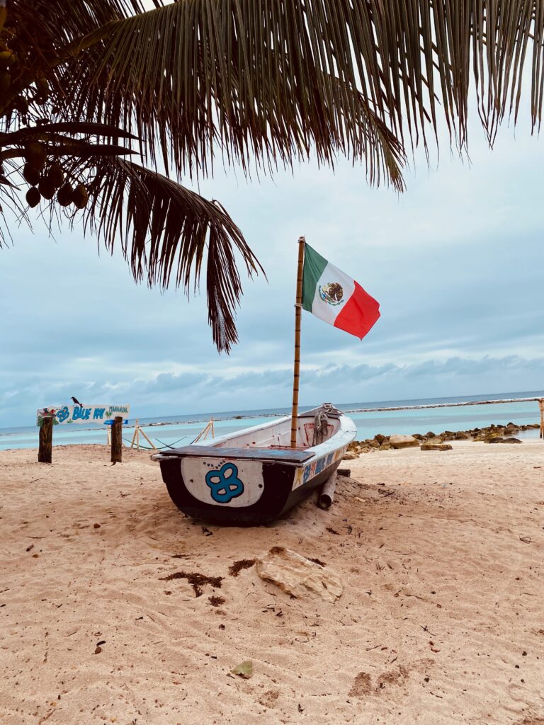 small boat on the beach with a Mexican Flag standing in it and the Caribbean Sea in the distance in Mahahual, Mexico
