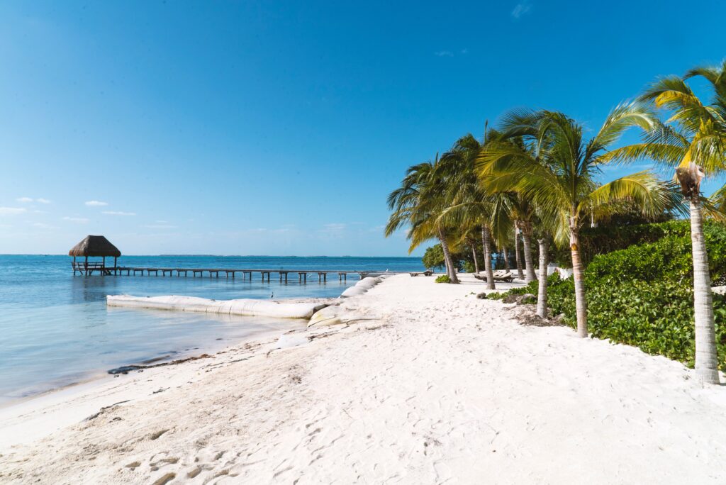 deserted quiet white sandy beach area with palm trees and a long deck featuring a palapa in Isla Mujeres, Mexico