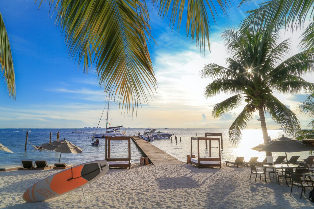 sunset setting beside palm trees and several beach lounge chairs with views of the Caribbean Sea at Zama Beach Club in Isla Mujeres