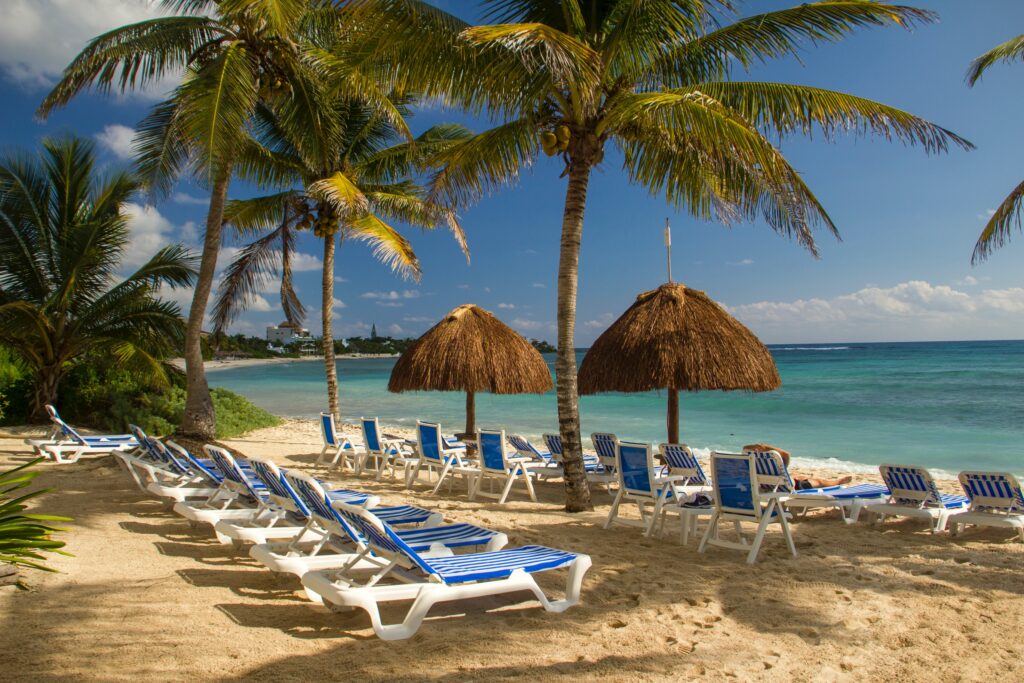 several beach loungers with palapas as umbrellas and palm trees at Akumal beach in Mexico