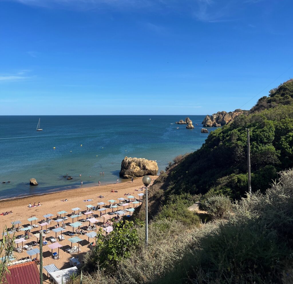 several beach lounge chairs and umbrellas at a popular beach with several unique rock formations on the water in Lagos, Portugal