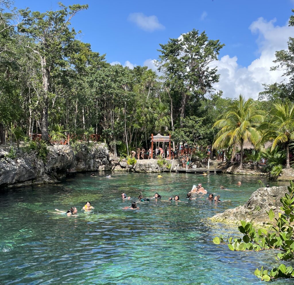several people swimming in a large open-air cenote at Casa Tortuga in Tulum, one of the best Tulum Excursions to do