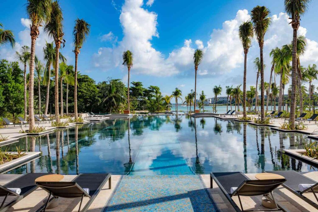 views of the large pool surrounded by palm trees and views of the ocean at the Conrad Tulum Riviera Maya resort