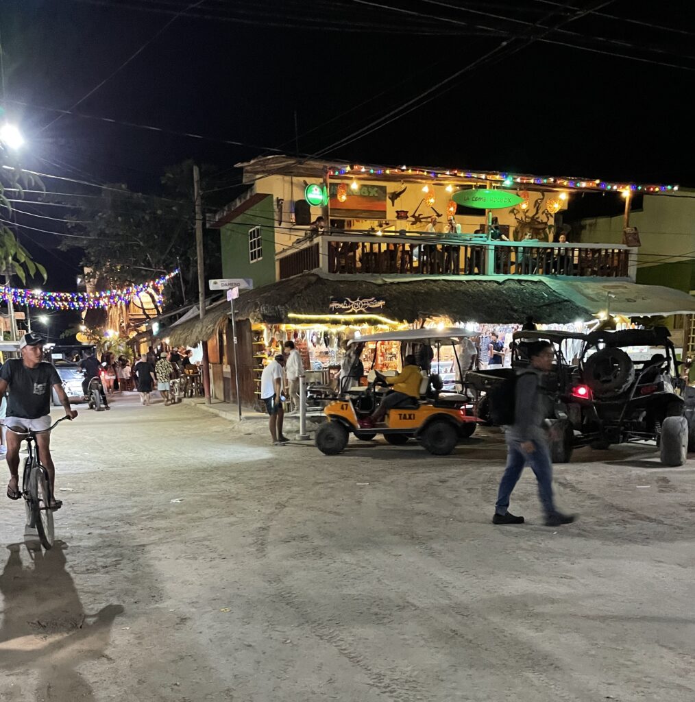 many tourists biking and driving golf carts and a bar in the background in Isla Holbox, Mexico