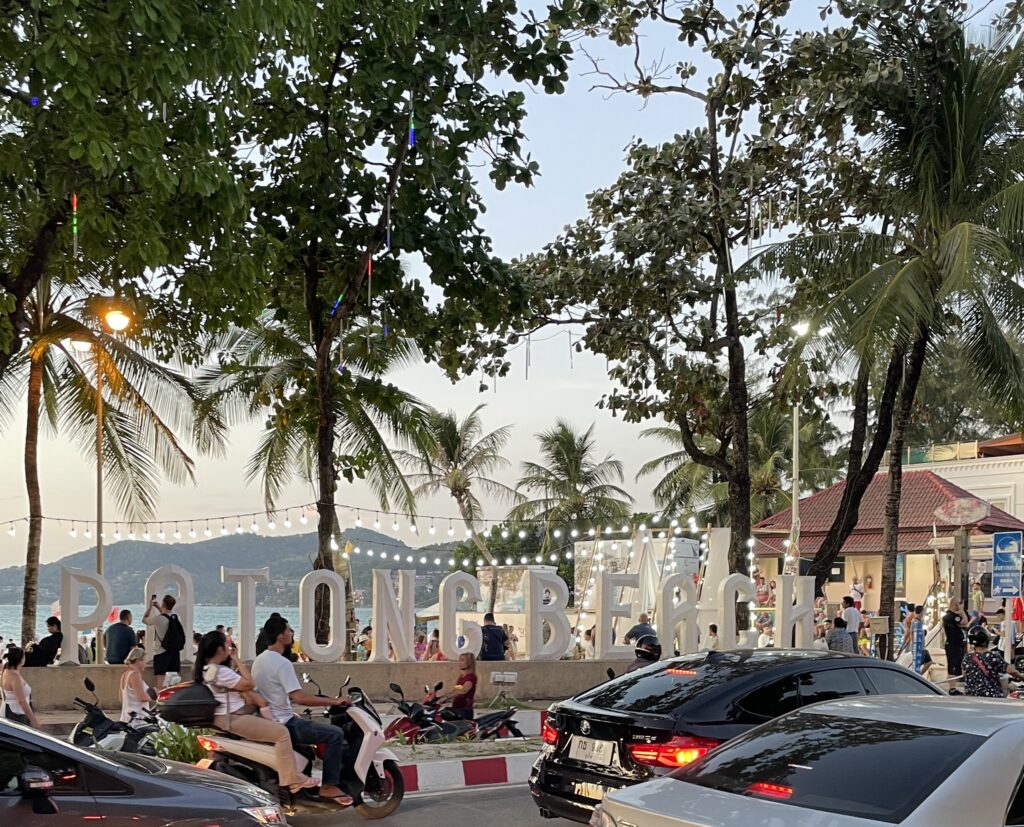 alternative white Patong Beach sign standing in front of Patong beach at sunset, surrounded by palm trees in Patong, Phuket
