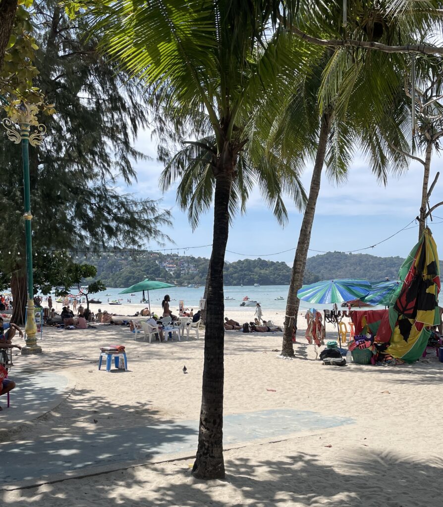 palm trees standing on a crowded Patong beach full of tourists in Phuket, Thailand