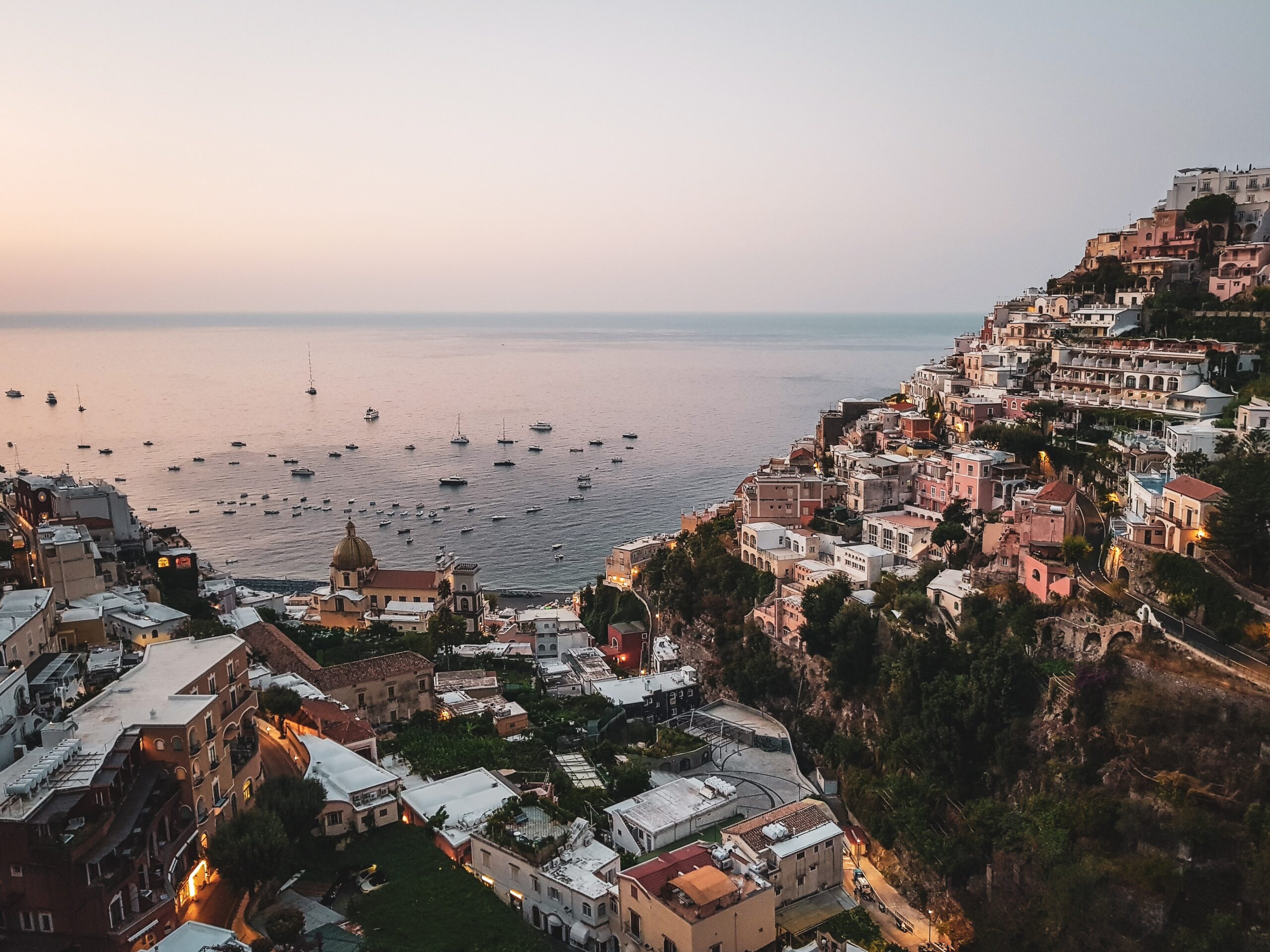 views of the hills of Positano with several boats anchored at the shores during sunset in Positano, Italy / is Positano expensive to visit