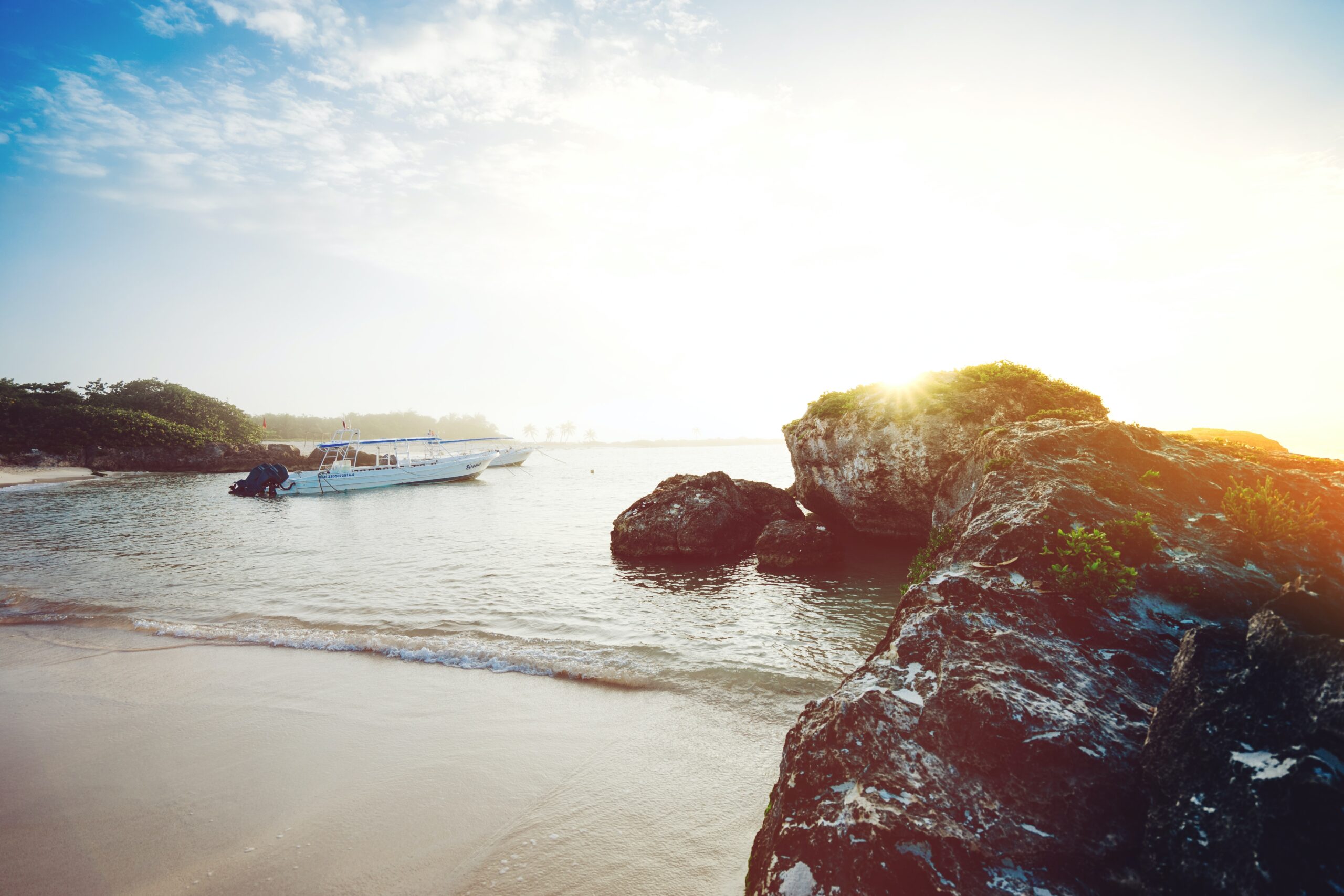 sun beaming in at sunset with a boat anchored on the shore at the beach in Akumal, Mexico