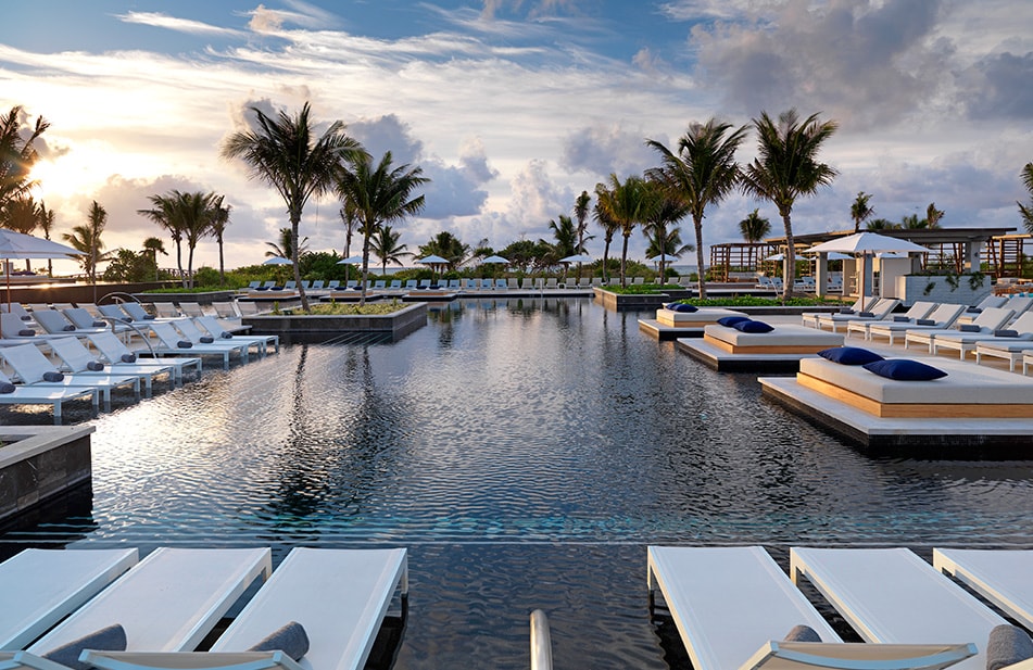 pool area surrounded by palm trees and the Caribbean Sea in the distance at the Unico Hotel Riviera Maya 