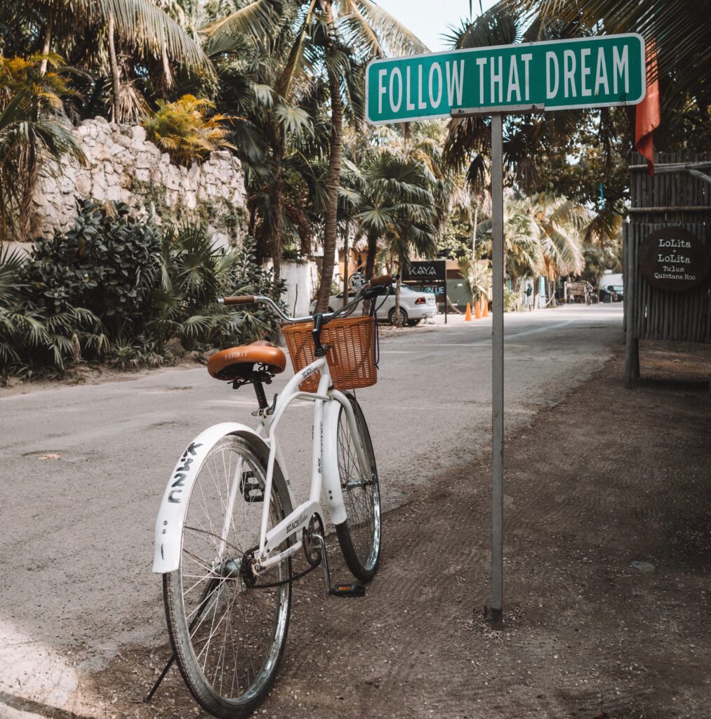 Bicycle stopped on the road by the famous "Follow That Dream" sign in Tulum, Mexico
