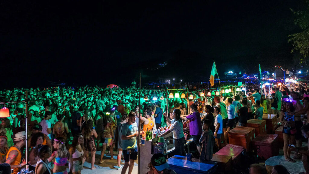 a beach at night full of tourists attending the famous Full Moon Party in Koh Phangan, Thailand