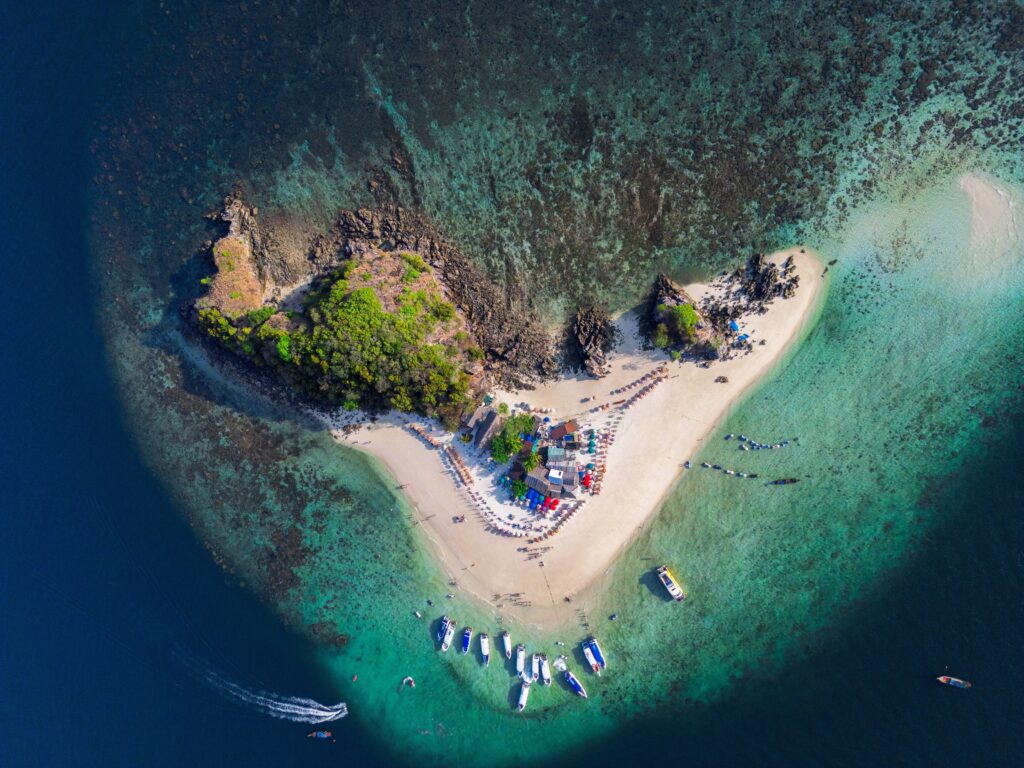 Aerial view of the small Khai Island in Phuket, showing several tourists at the island, boats docked, and a clear visual of the entire island from above