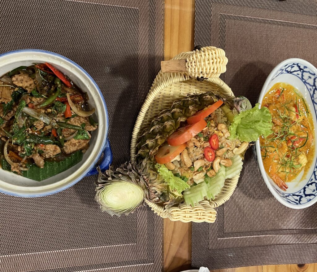 table full of Thai Dishes, Pad Kra Pow, pineapple friend rice, and coconut curry with rice being served at Pinto / Best Kata Beach restaurants