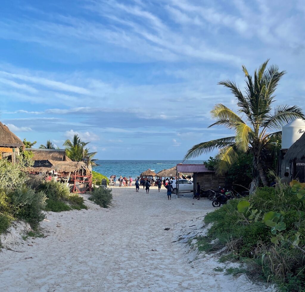 a sandy trail leading to the Tulum North Beach area showing clear blue skies, palm trees and turquoise blue waters